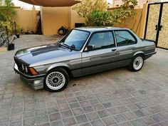 an old bmw is parked in front of a house with its door ajar open