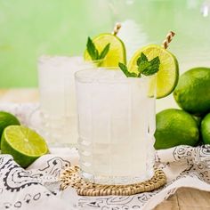 two glasses filled with lemonade and limes on a table next to some limes