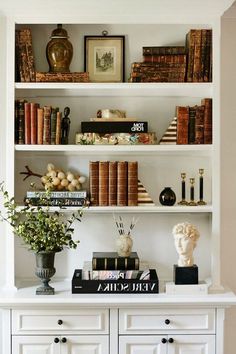 a white book shelf filled with books next to a vase and busturifit