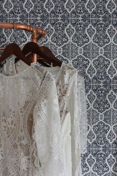 a white blouse hanging on a wooden hanger in front of a wallpapered background