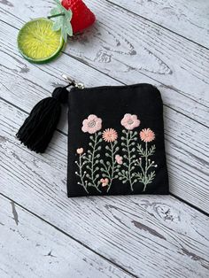 a small black pouch with flowers and tassels next to a strawberries on a white wooden table