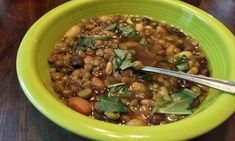 a green bowl filled with beans and greens on top of a wooden table next to a cup