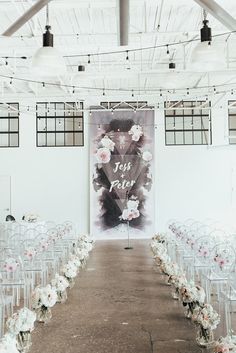 an aisle with clear chairs and white flowers on the side is lined up in front of a large poster