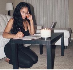 a woman is sitting on the floor writing in front of a coffee table with a candle