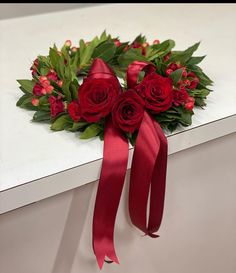 a bouquet of red roses and greenery on a white surface with a ribbon tied around it