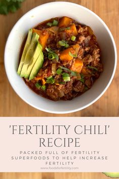 a white bowl filled with chili and avocado on top of a wooden table