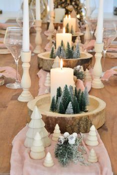 a wooden table topped with white candles and evergreen trees on top of pink napkins