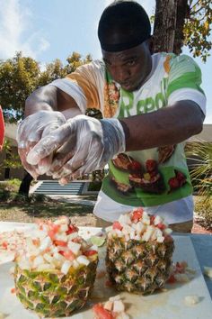 a man cutting up food on top of a wooden table next to a pineapple