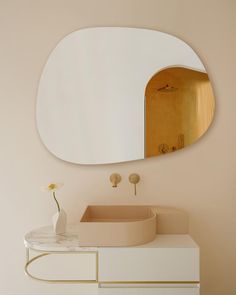 a white sink sitting under a mirror next to a vase with a flower in it