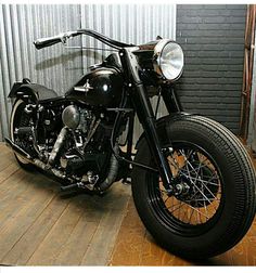 a black motorcycle parked on top of a wooden floor next to a metal garage door