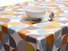 a bowl and spoon sitting on top of a colorful table cloth with an abstract design