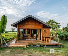 a small wooden house sitting in the middle of a lush green field next to a banana tree