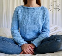 a woman sitting on top of a bed wearing a blue knitted sweater and jeans