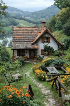 a house in the middle of a garden with flowers around it and a path leading up to it