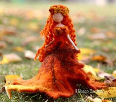 a doll is sitting in the grass with leaves around her and she has long red hair