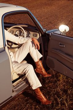 a man sitting in the driver's seat of a car with his foot on the dashboard