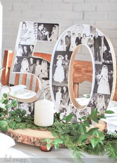 a wooden table topped with photos and greenery next to a white candle on top of a