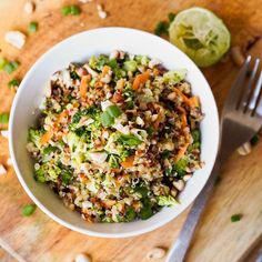 a white bowl filled with broccoli, carrots and other food on top of a wooden table