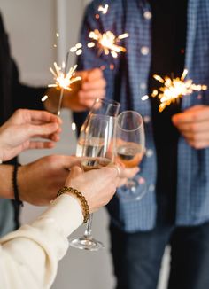 people holding wine glasses with sparklers in their hands