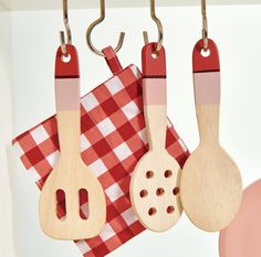 three wooden utensils hanging from hooks on a red and white checkered table cloth