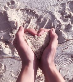 two hands holding sand in the shape of a heart