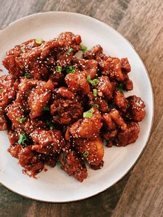 a white plate topped with meat covered in sauce and green onions on top of a wooden table