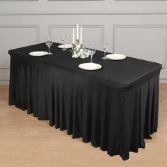 a black table cloth with white plates and candles on it in front of a wall