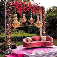 a pink couch sitting on top of a lush green field next to a flower covered arbor