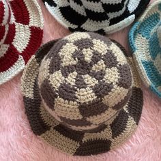 four crocheted hats are laying on a pink surface, one is brown and the other is white