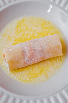 a piece of food on a white plate with yellow liquid in the bowl next to it