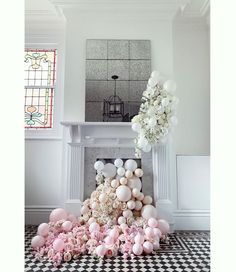 a bunch of balloons and flowers on the ground in front of a fireplace with a mirror above it