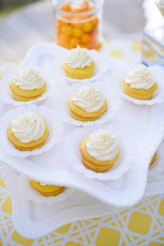 cupcakes with white frosting sitting on a tray next to some candy jars