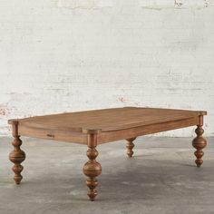 an old wooden table in front of a white brick wall with wood legs and feet