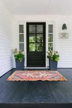 a black front door with two planters and a rug on the ground in front of it