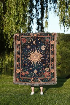 a woman standing in the grass holding up a blanket with an image of the sun and moon on it