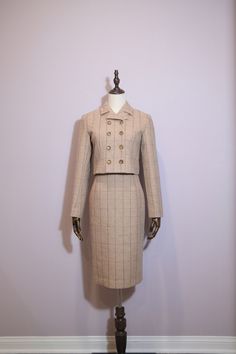 Features: - Elegant beige plaid fabric with subtle lines. - Six decorative buttons in two rows on the jacket. - Cropped jacket for a contemporary twist on a classic style. - High-waisted pencil skirt to elongate and enhance your silhouette. - Perfect balance of vintage charm and modern sophistication. - Versatile style suitable for a variety of occasions. Composition: 80% Wool 20%Polyester Care: Suggested dry clean only to maintain fabric integrity. Elegant Beige Buttoned Skirt, Elegant Beige Skirt With Buttons, Fitted Buttoned Formal Skirt, Classic Fitted Beige Skirt Suit, Classic Beige Fitted Skirt Suit, Beige Fitted Skirt Suit For Fall, Formal Fitted Skirt With Buttons, Beige Plaid, High Waisted Pencil Skirt