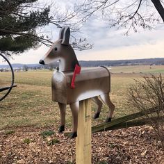 a metal horse statue sitting on top of a wooden post next to a tree in a field