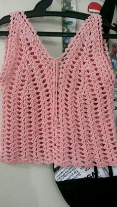 a pink crocheted top hanging on a clothes hanger next to a magazine rack