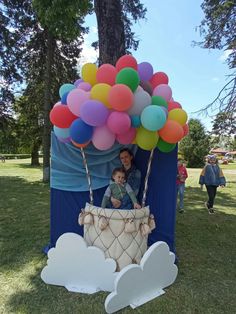 a woman and her child in a balloon cart at an outdoor event with balloons floating over them