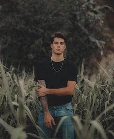 a man standing in the middle of a corn field with his arms crossed and looking off into the distance