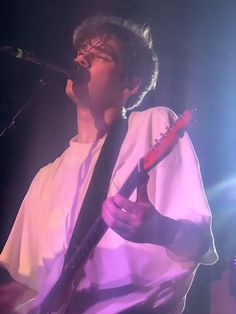 a man holding a guitar while standing in front of a microphone