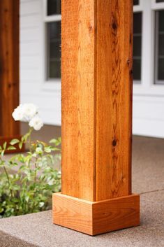 a wooden post in front of a house with white flowers growing on the ground next to it