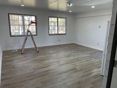 an empty room with two windows and a ladder in the foreground, next to a wall that has been painted white