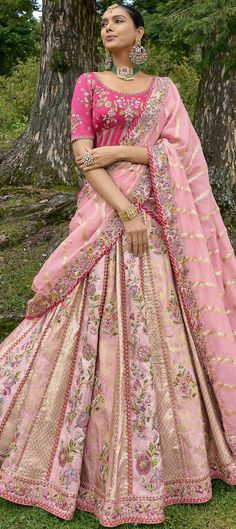 a woman wearing a pink and gold lehenga in front of a large tree