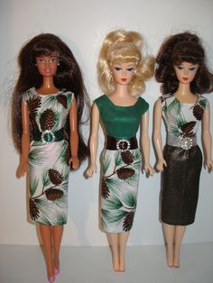 three barbie dolls standing next to each other in front of a white wall with pine cones on it