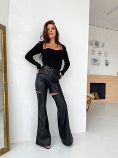 a woman standing in front of a mirror with her hands on her hips wearing black leather pants