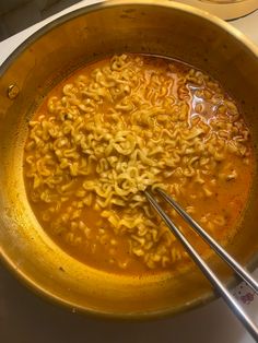 the bowl is full of noodles and soup with two tongs in it, ready to be eaten