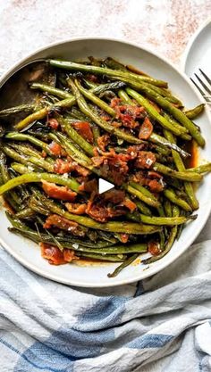 a white plate topped with green beans covered in sauce next to a fork and knife