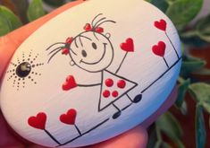 a hand holding a painted rock with a girl and hearts on it