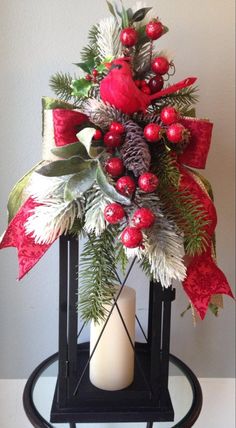 a red and white christmas wreath on top of a black stand with pine cones, holly berries and evergreen leaves